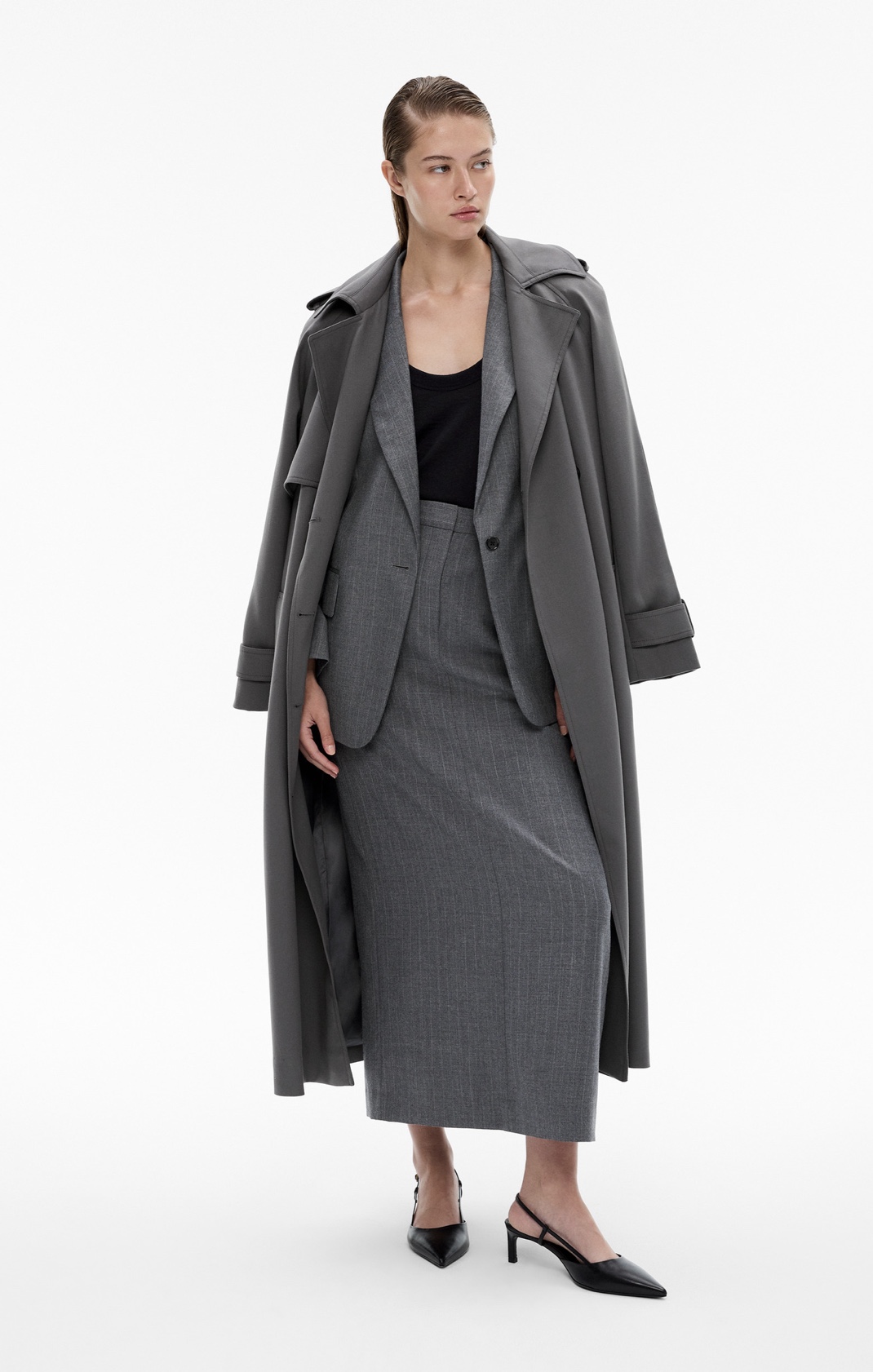 Woman in grey trench coat, grey blazer, black tank, grey midi skirt and black point heels