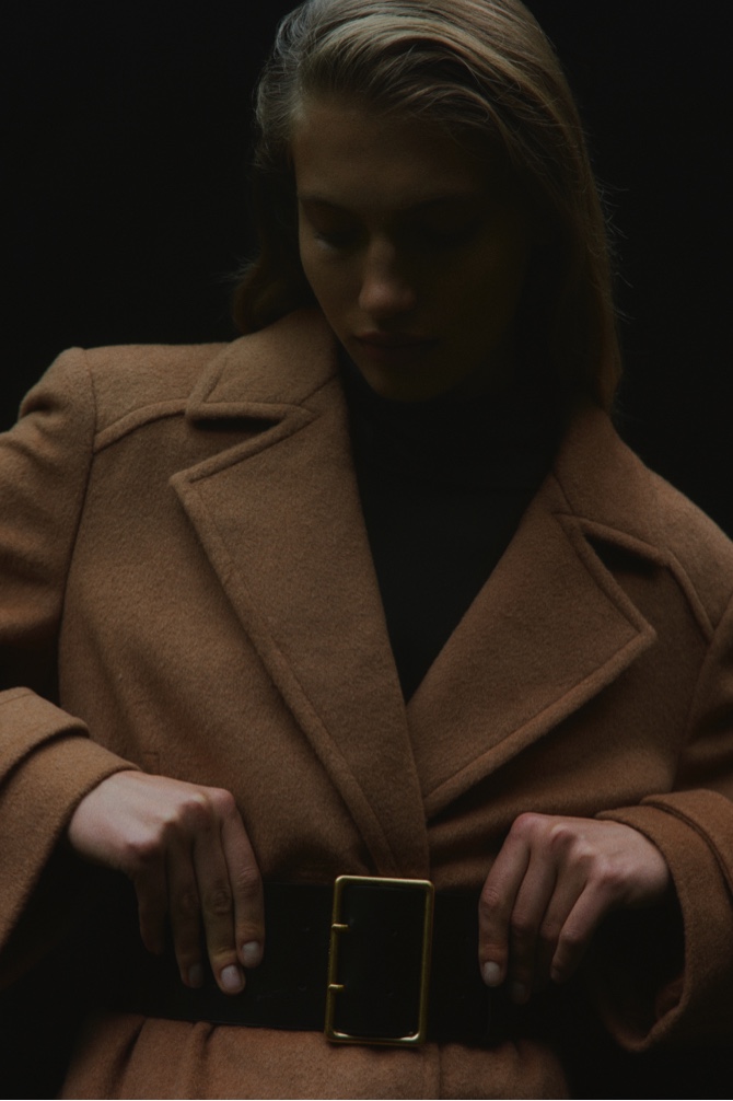 Woman in the golden brown wool cashmere tie coat, black drape neck long sleeve blouse and black wide fastened belt
