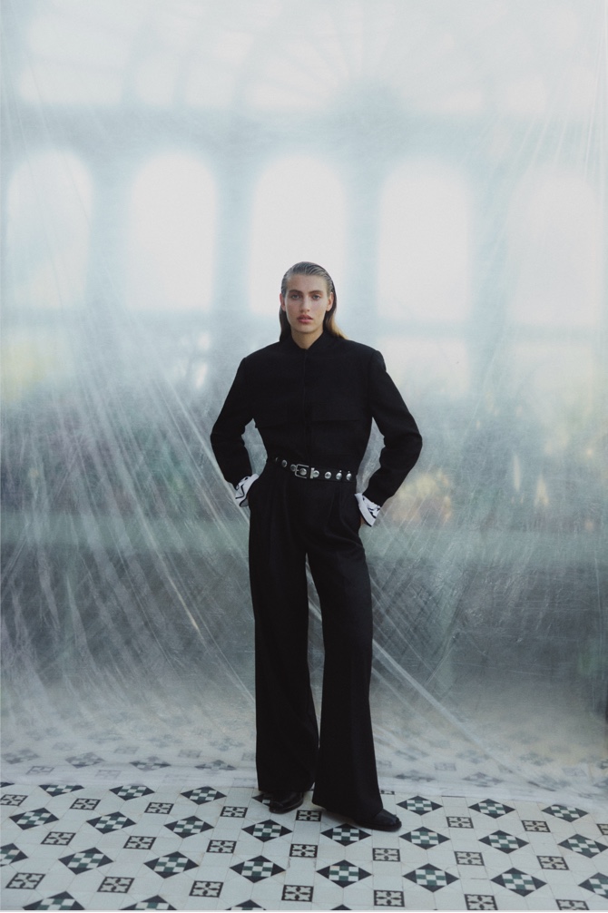 Woman in black structured bomber, stripe top, black wool blend relaxed rise trouser and black studded leather belt