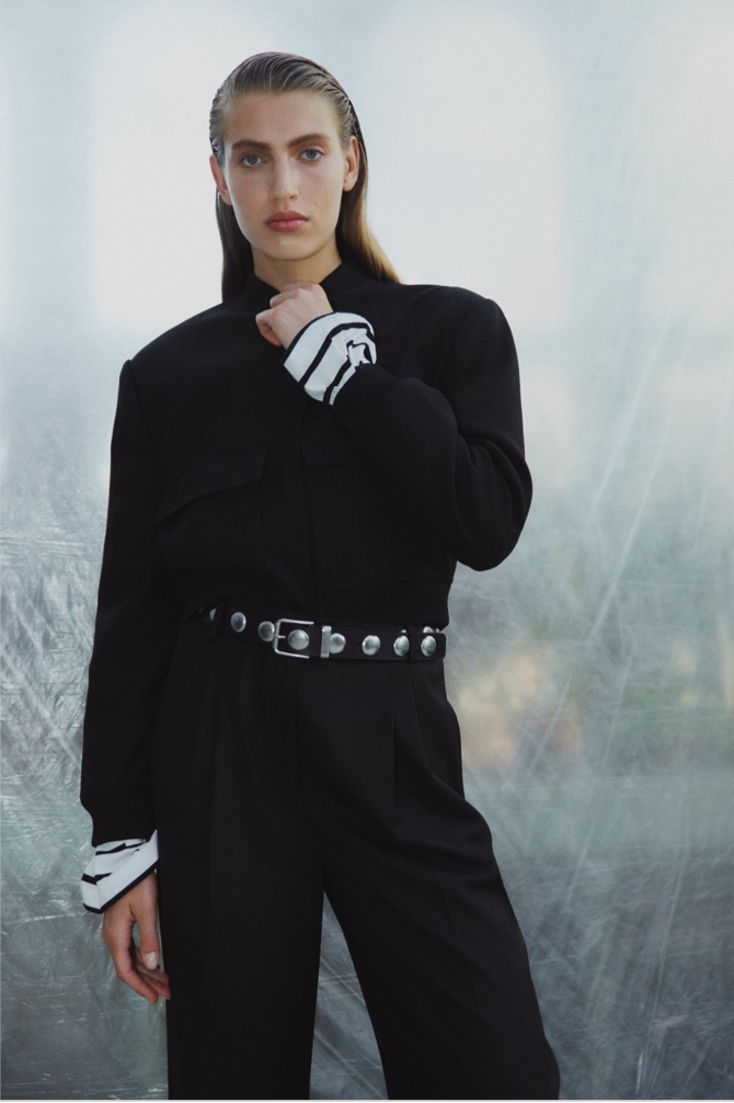 Woman in black structured bomber, stripe top, black wool blend relaxed rise trouser and black studded leather belt