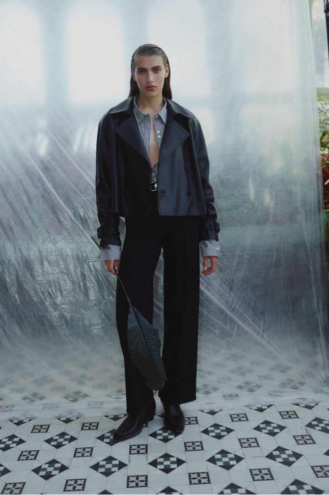 Woman in black leather trench jacket, black cotton stripe relaxed shirt, washed black pinstitch slim jean and black studded leather belt
