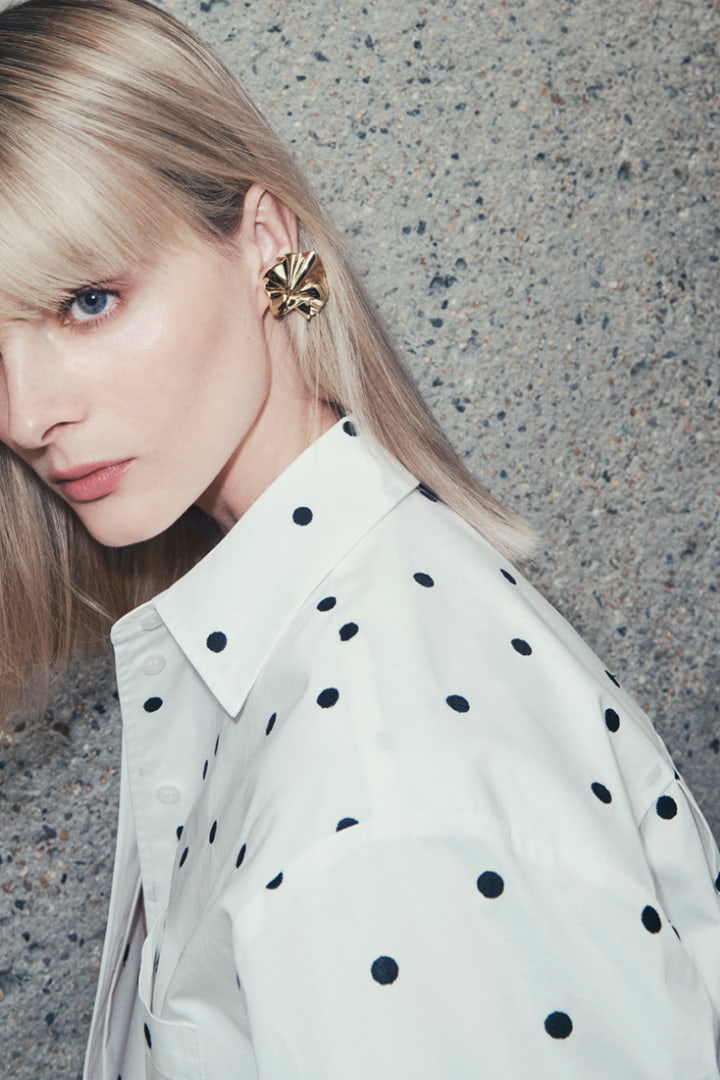 Woman in white embroidered spot shirt and gold clara clip-on earring