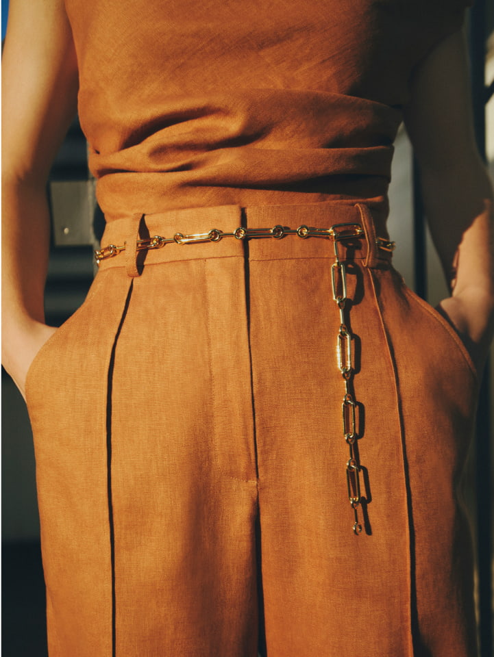 Woman in nutmeg off shoulder top, nutmeg high rise pants, gold elle chain belt