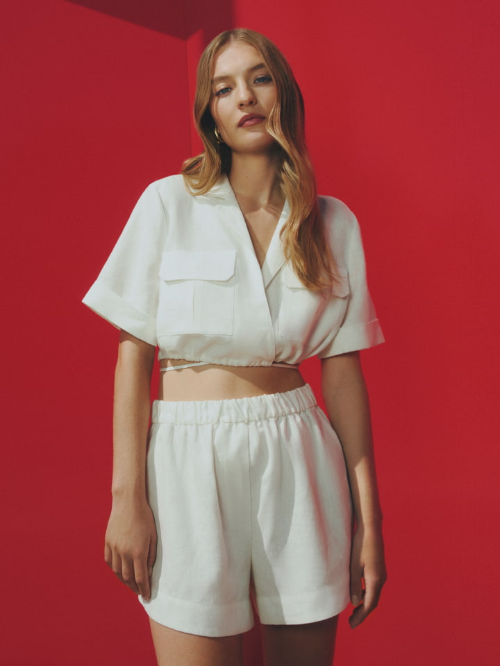 Woman in white utility tie shirt and white linen pull on short