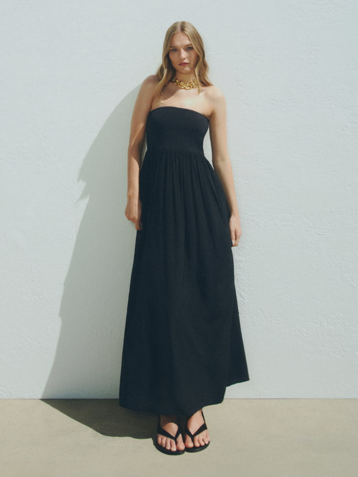 Woman in black strapless bodice dress, black jade sandals, gold zahra necklace and gold elliot crystal necklace
