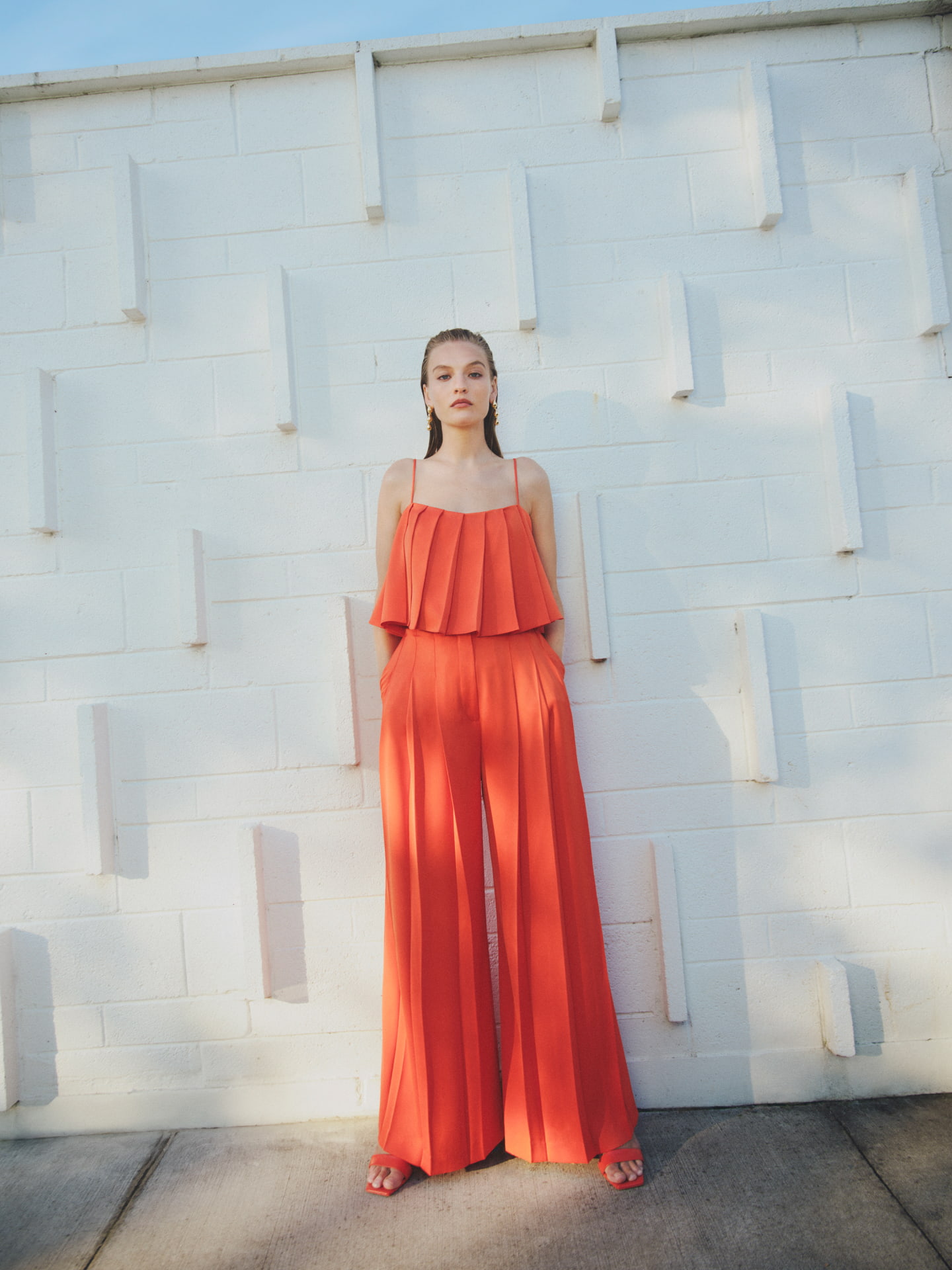 Woman in tangerine pleat camisole, tangerine pleat pant and tangerine grace mule