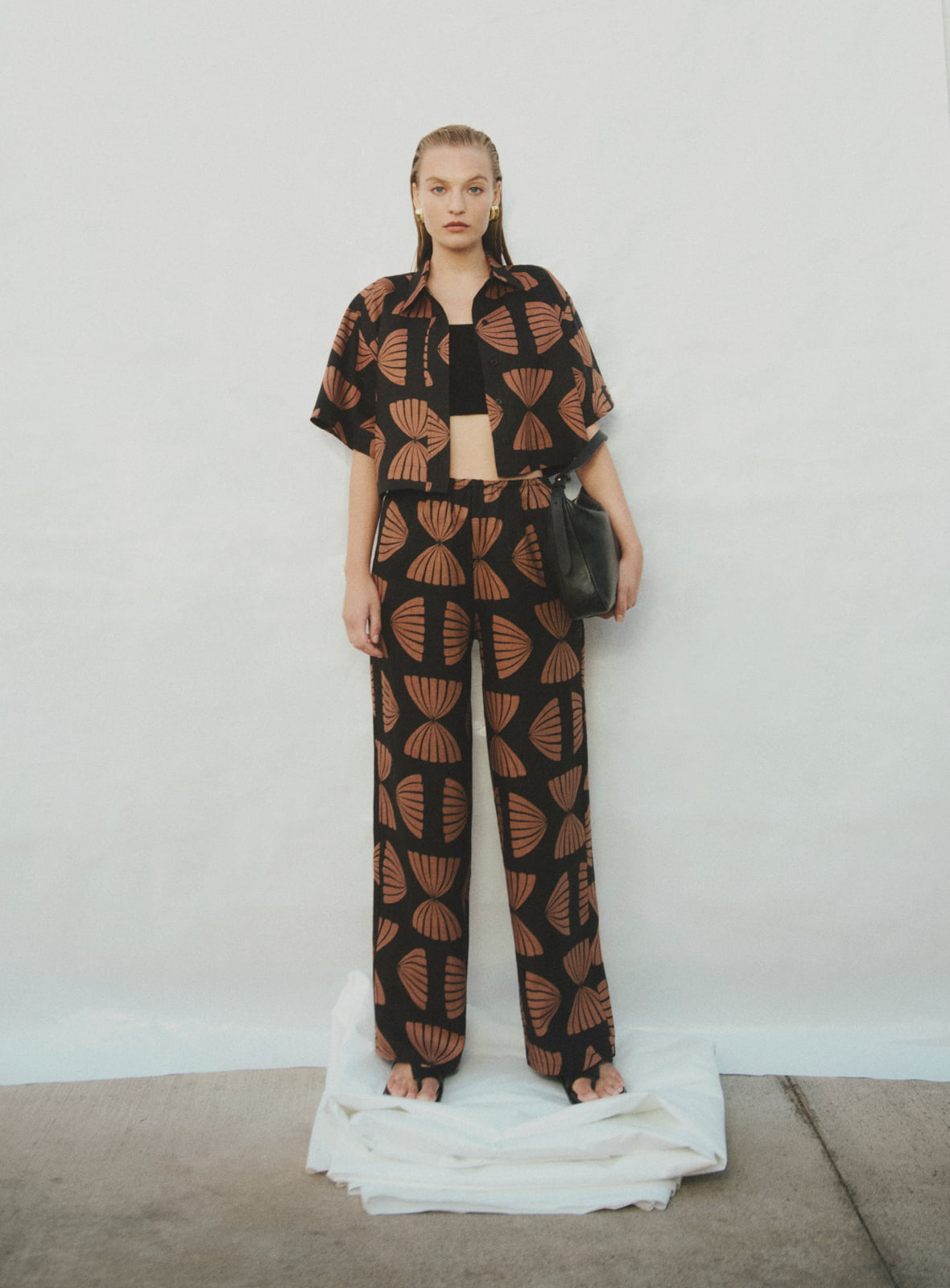 Woman in nutmeg print linen crop shirt, nutmeg print pull on pant, black cropped rib knit top, black billie sandal and black jodie leather bag