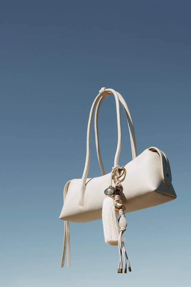 Cream leather handbag with tassel charm floating against a blue sky