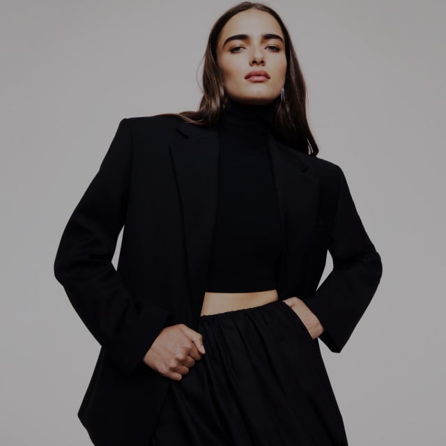 Woman in black high neck crop, black oversized blazer and black bubble skirt